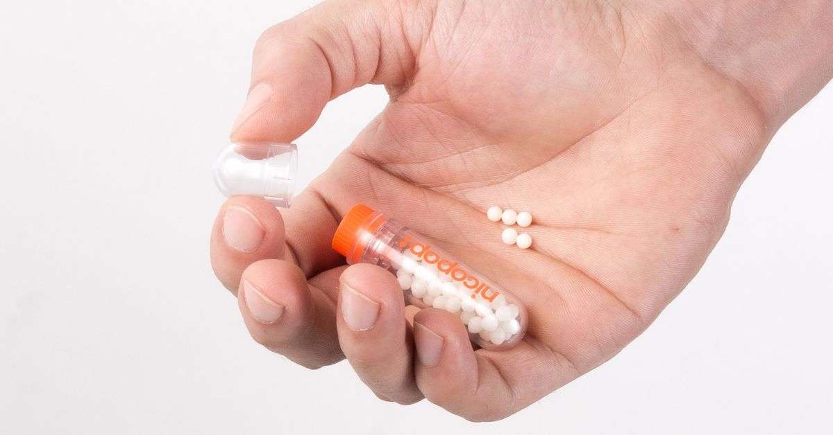 A person's hand holding a small orange tube labeled 'Nicopop' with white nicotine pearls spilling into the palm