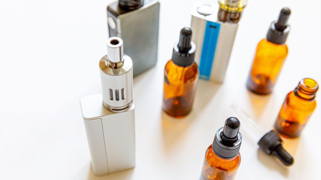 Several vapes on a table with bottles of liquid nicotine next to the,. 
